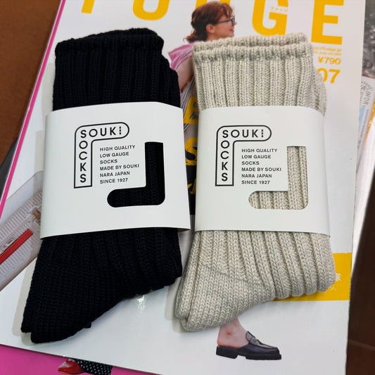 Two pairs of socks, one black and one beige, with SOUK! branding on a magazine background.
