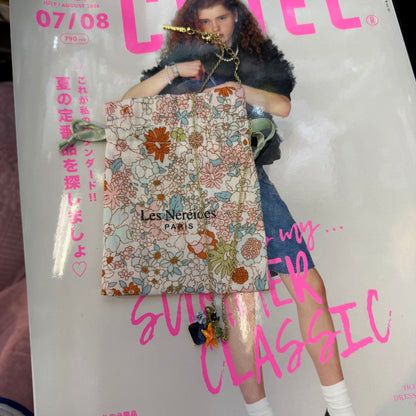 A fashion magazine cover featuring a woman holding a floral patterned shopping bag with the brand name 'Les Nerdices Paris' printed on it. The cover has prominent pink text and a white background.