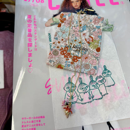A fashion magazine or booklet featuring a floral-patterned pouch and a gold-tone necklace with a pink and gold pendant, displayed over printed illustrations and pink Japanese text.