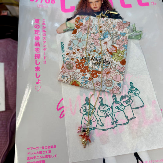 A fashion magazine or booklet featuring a floral-patterned pouch and a gold-tone necklace with a pink and gold pendant, displayed over printed illustrations and pink Japanese text.