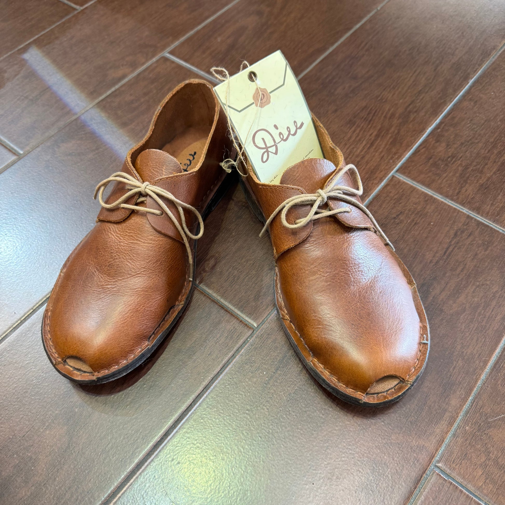 Pair of brown leather shoes on a tiled floor with a visible brand tag.