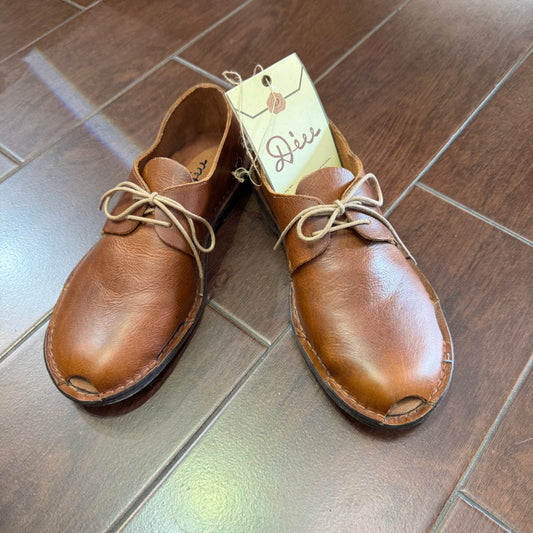 Pair of brown leather shoes on a tiled floor with a visible brand tag.